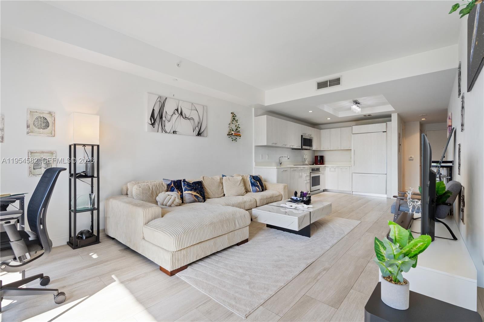 A modern open-concept living room features a sectional sofa, coffee table, and adjacent kitchen area — 55 SW 9th St # 3005, Miami FL 33130, MIAMI, FL