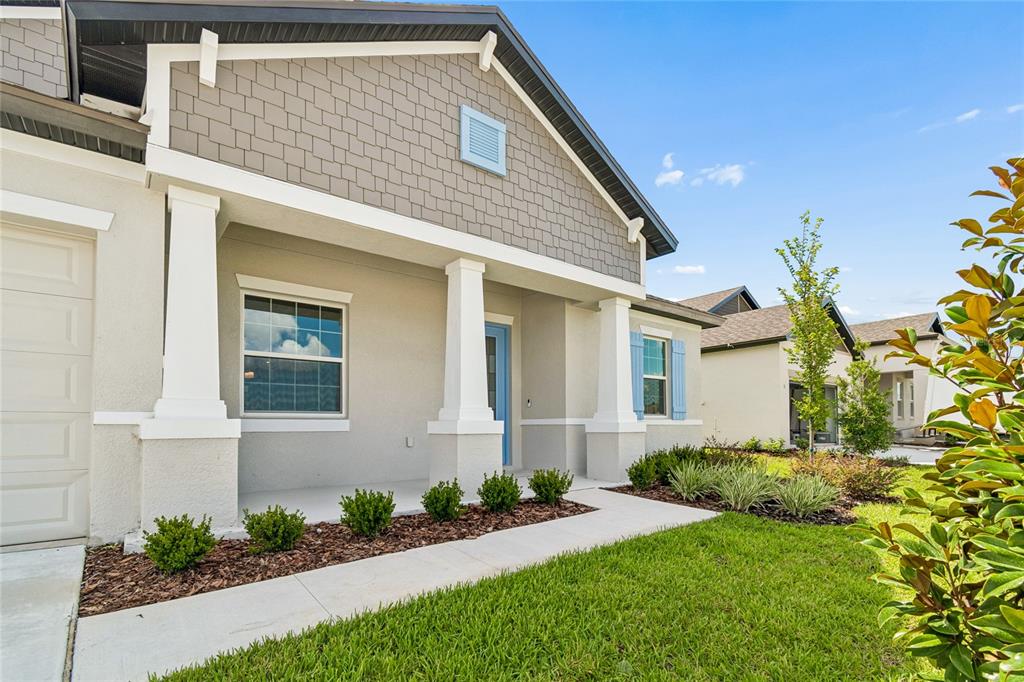 A single-story house exterior features a covered porch, light-colored stucco, and gray shingle siding — 12610 KELLY ANN LOOP, BROOKSVILLE, FL