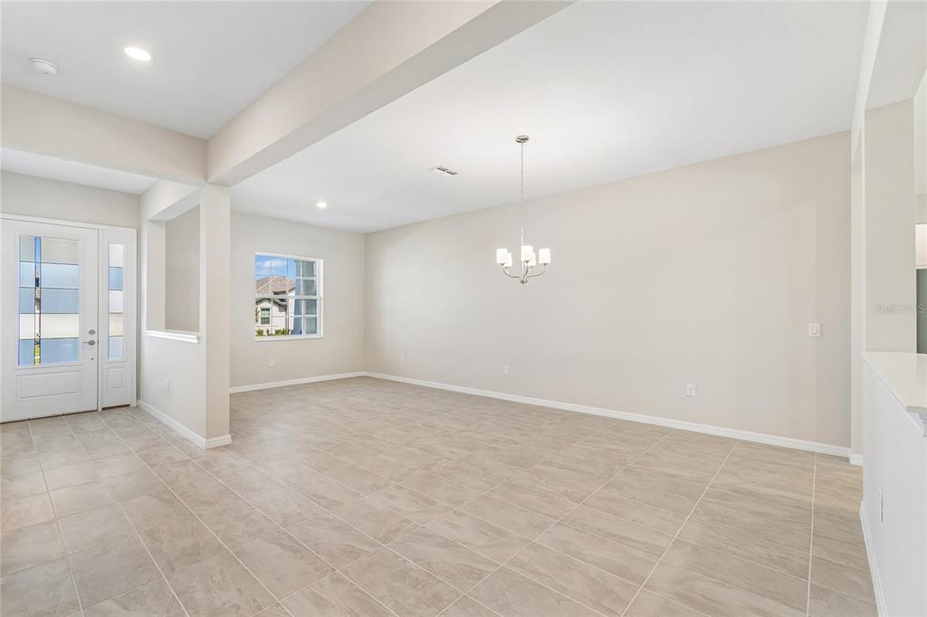 An empty dining room features light-colored tile flooring, a chandelier, and a front entry door — 12610 KELLY ANN LOOP, BROOKSVILLE, FL