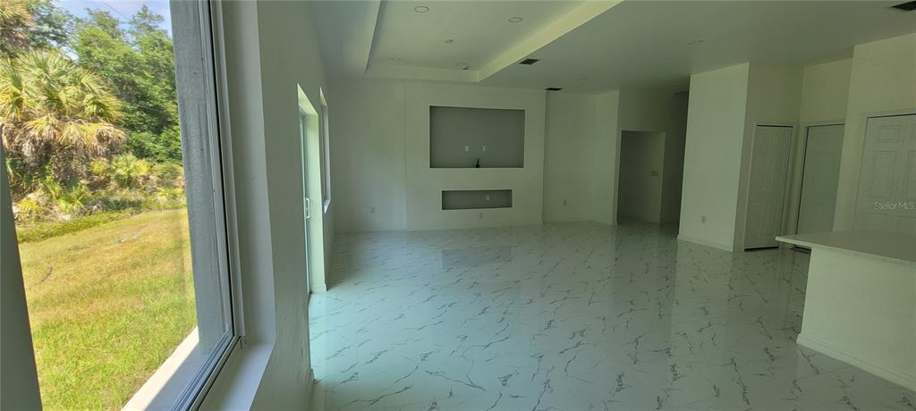 An open-concept living room features white marble-look tile flooring and a recessed media wall — 26248 EAGER ROAD, PUNTA GORDA, FL