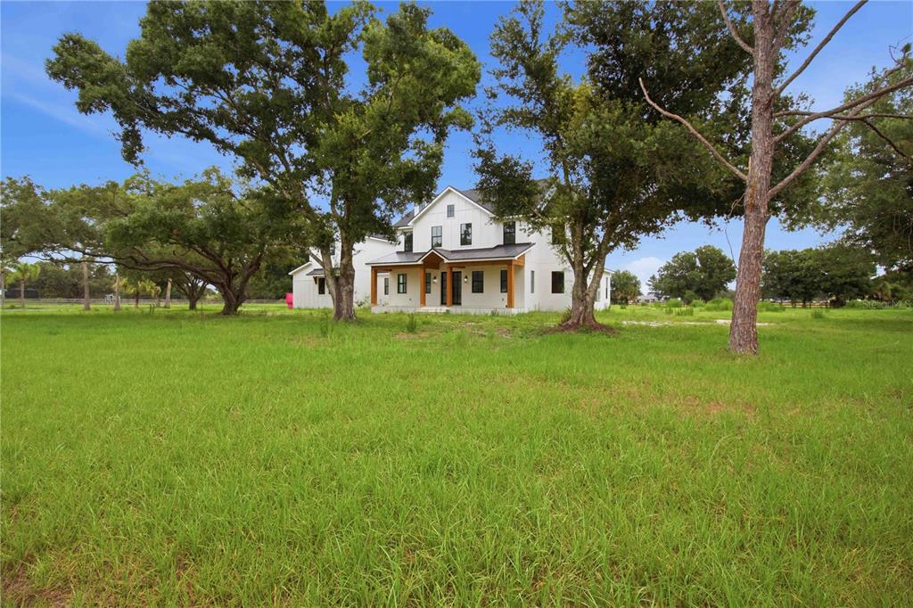 A white two-story farmhouse with a wooden porch sits in a large grassy field — 639 OAKFORD ROAD, SARASOTA, FL