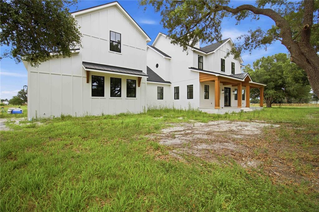 A modern white farmhouse with black window frames and a wooden porch sits on grass — 639 OAKFORD ROAD, SARASOTA, FL