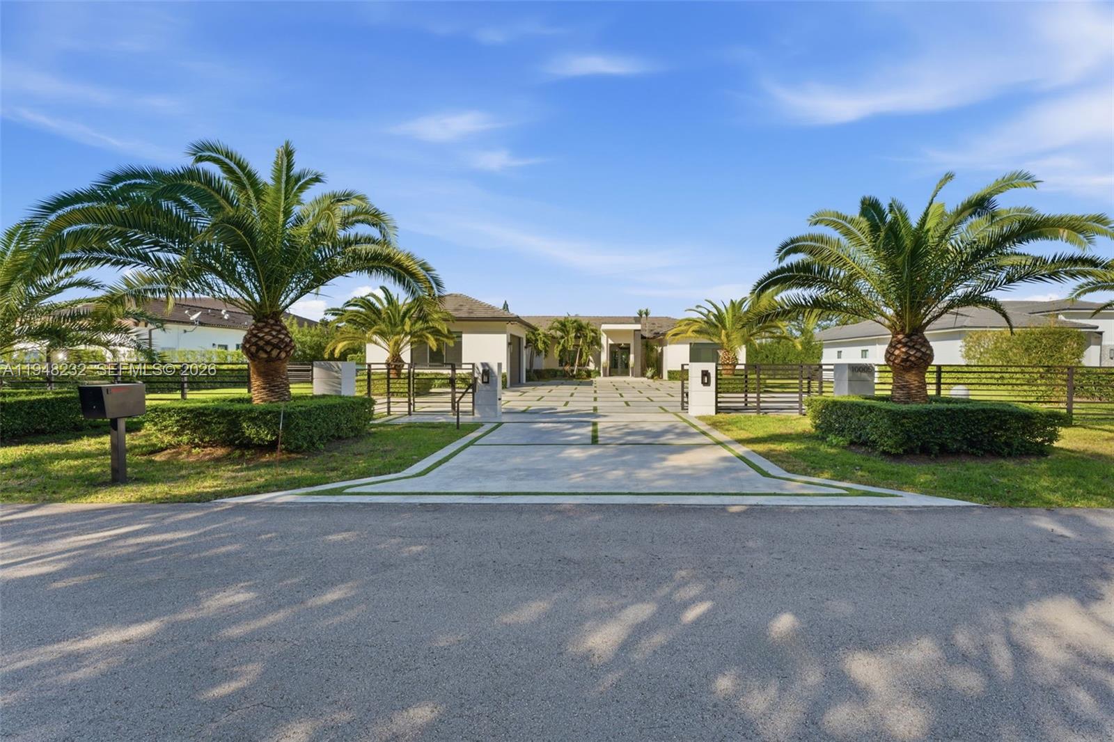 A modern single-story house with a large concrete driveway and palm trees at sunset — 10005 SW 66th St, Miami FL 33173, MIAMI, FL