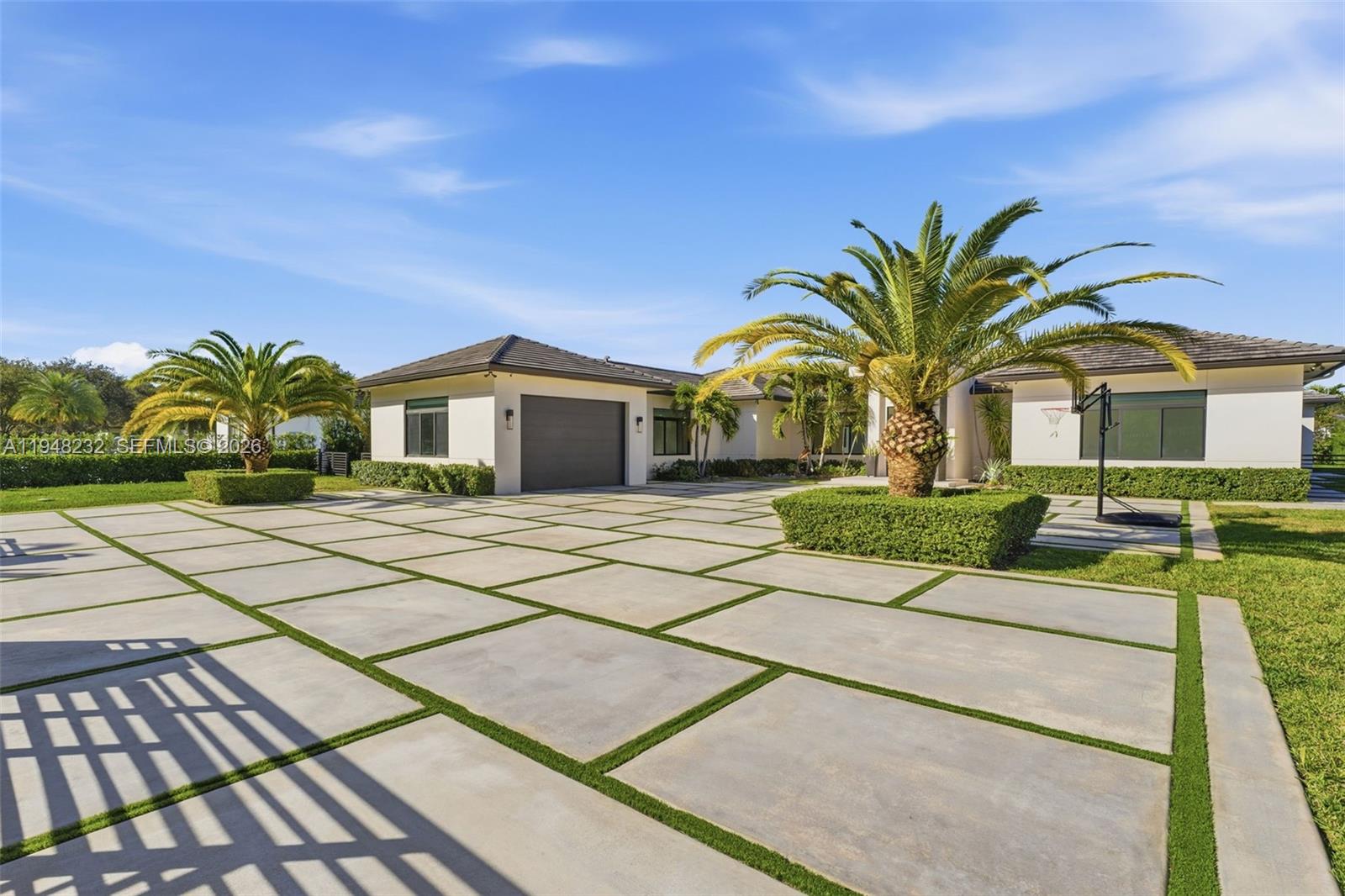A modern house features a large concrete paver driveway with grass strips and palm trees — 10005 SW 66th St, Miami FL 33173, MIAMI, FL