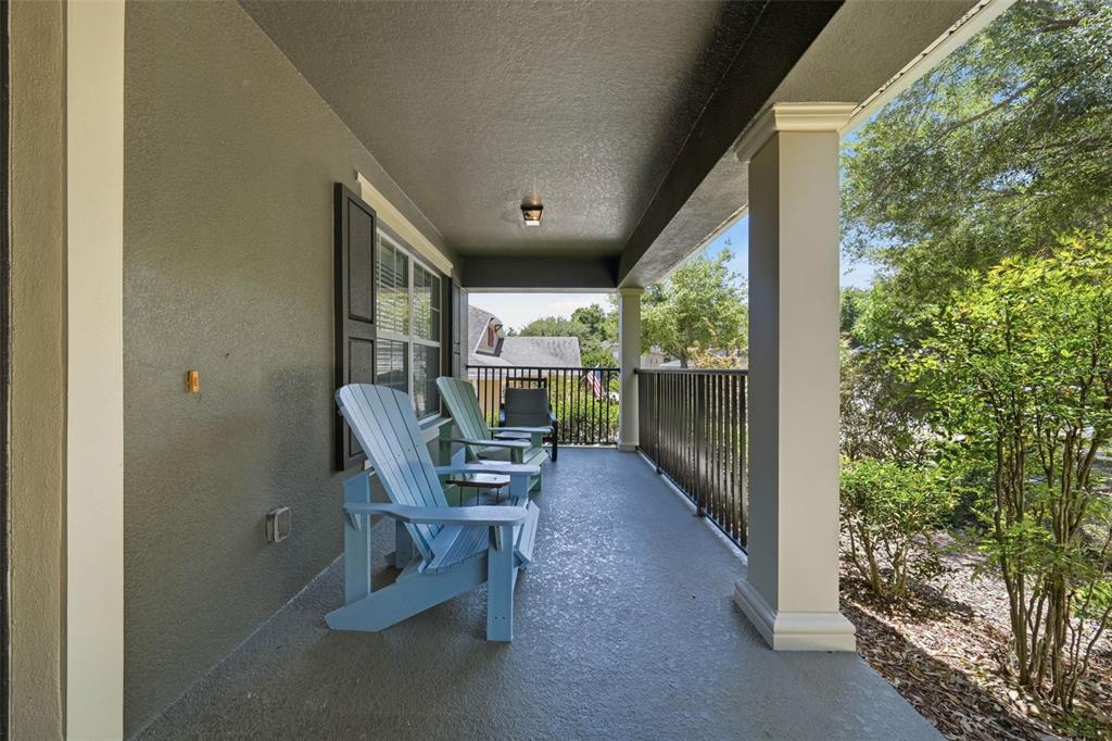 A covered porch features light blue Adirondack chairs, a dark metal railing, and beige columns — 20831 SULLIVAN RANCH BOULEVARD, MOUNT DORA, FL