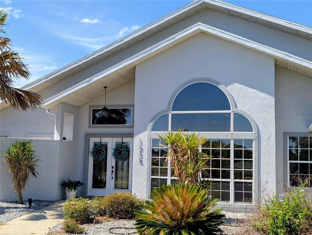 The exterior of a light-colored house features a large arched window and double front doors — 1235 E HARTFORD STREET, HERNANDO, FL