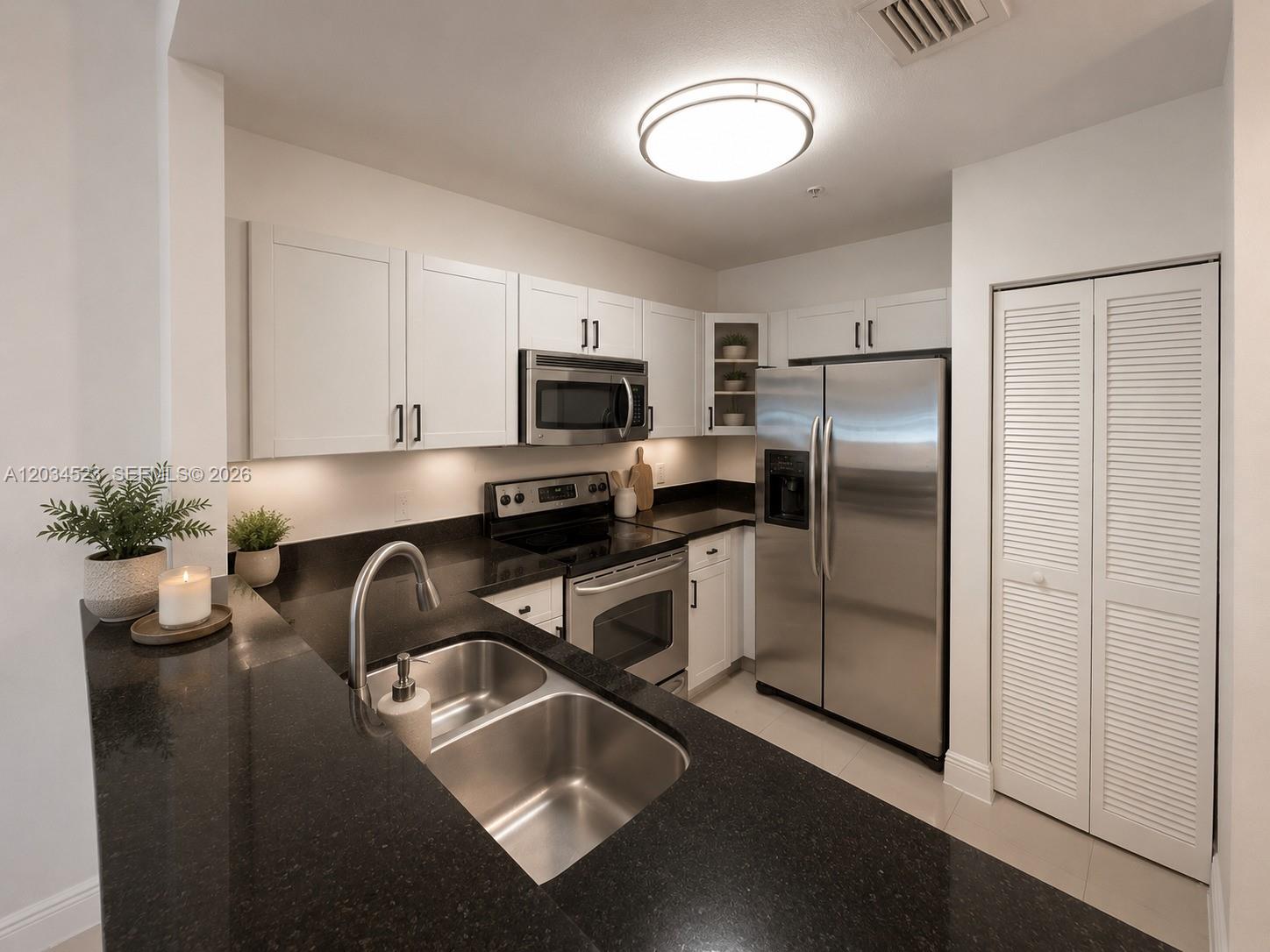 A kitchen features white cabinets, black countertops, stainless steel appliances, and a double-basin sink — 652 NE 63rd St # 105, Miami FL 33138, MIAMI, FL