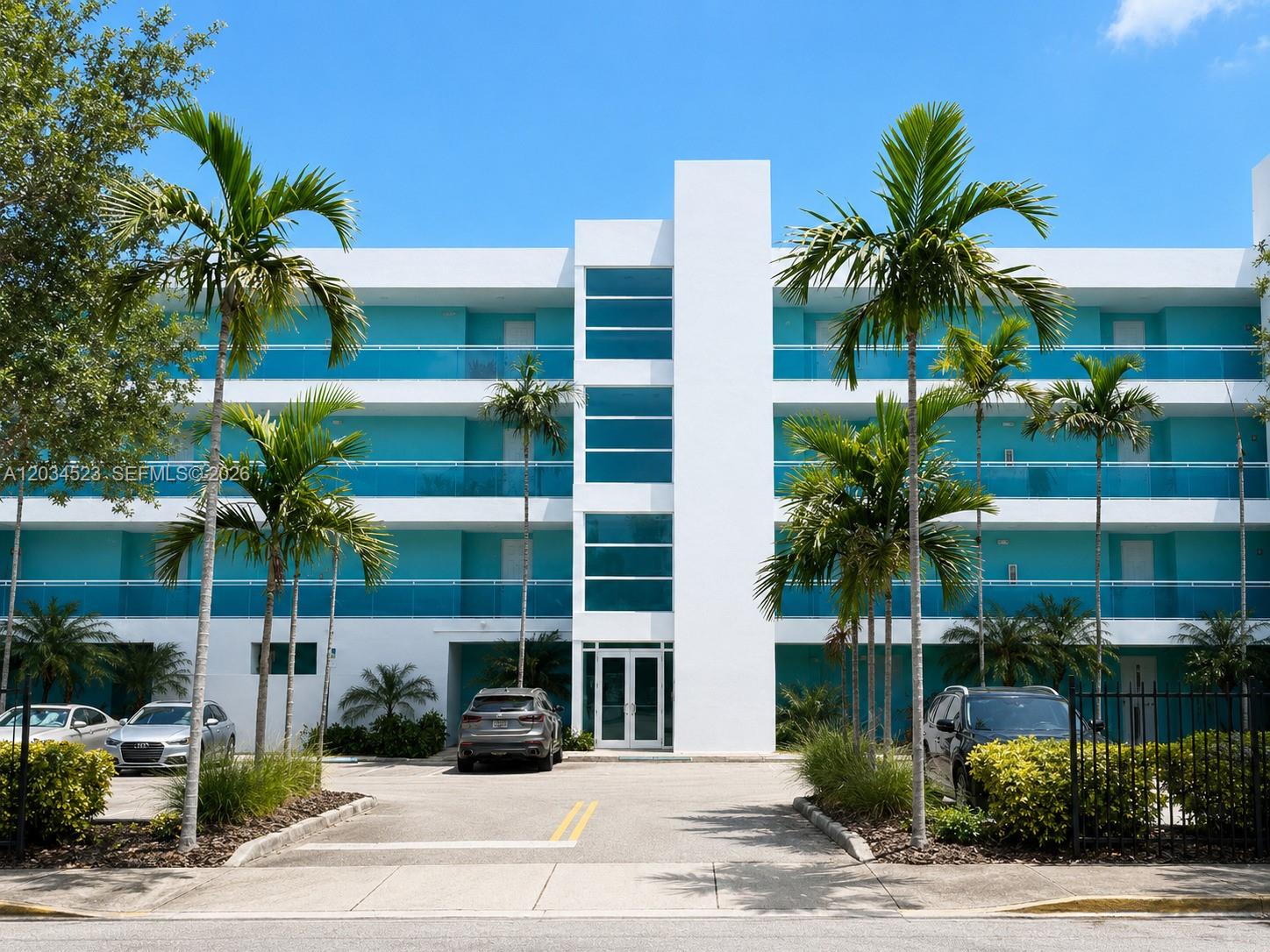A three-story white building with turquoise balconies and palm trees in the foreground — 652 NE 63rd St # 105, Miami FL 33138, MIAMI, FL