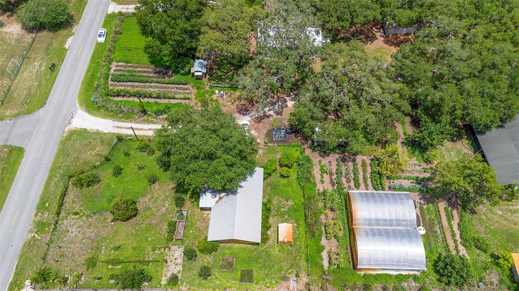 A teal metal building with a covered patio and brick pavers sits in a wooded yard — 2026 LEWIS ROAD, LEESBURG, FL