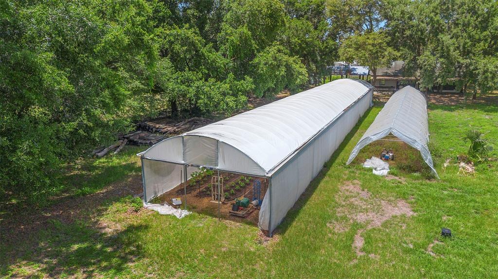 An aerial view of a double-tunnel greenhouse situated in a lush, cultivated garden — 2026 LEWIS ROAD, LEESBURG, FL