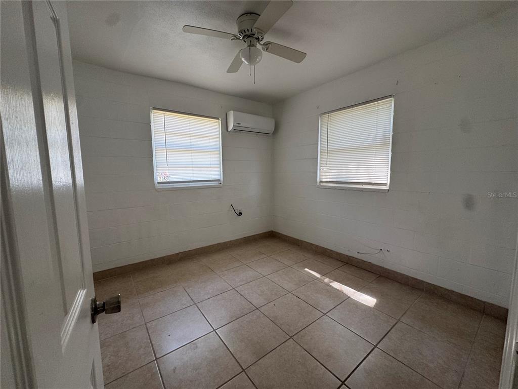 An empty room features white block walls, tiled floors, a ceiling fan, and a wall-mounted AC — 1715 1/2 MARTIN LUTHER KING JR BOULEVARD, BARTOW, FL
