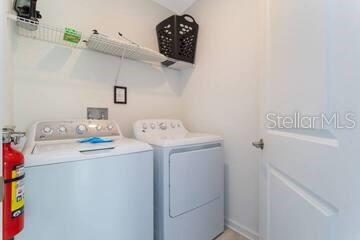 A laundry room features a white washer and dryer with a wire shelf above — 989 SPLASH SHOT PLACE UNIT ., DAVENPORT, FL