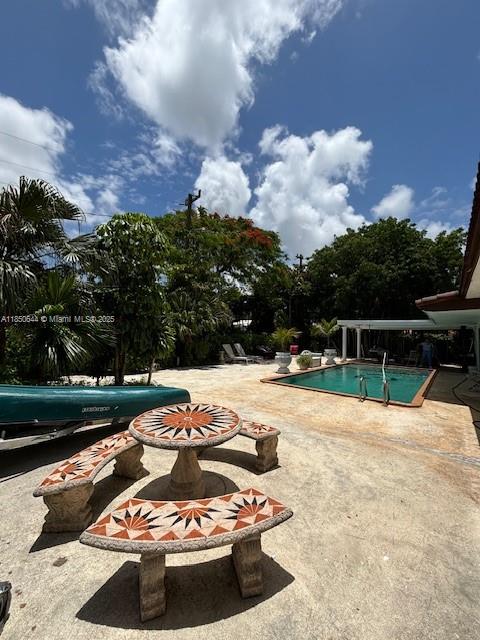A patio features a stone table and benches next to a swimming pool and boat — 6440 Miller Dr, South Miami FL 33155, SOUTH MIAMI, FL