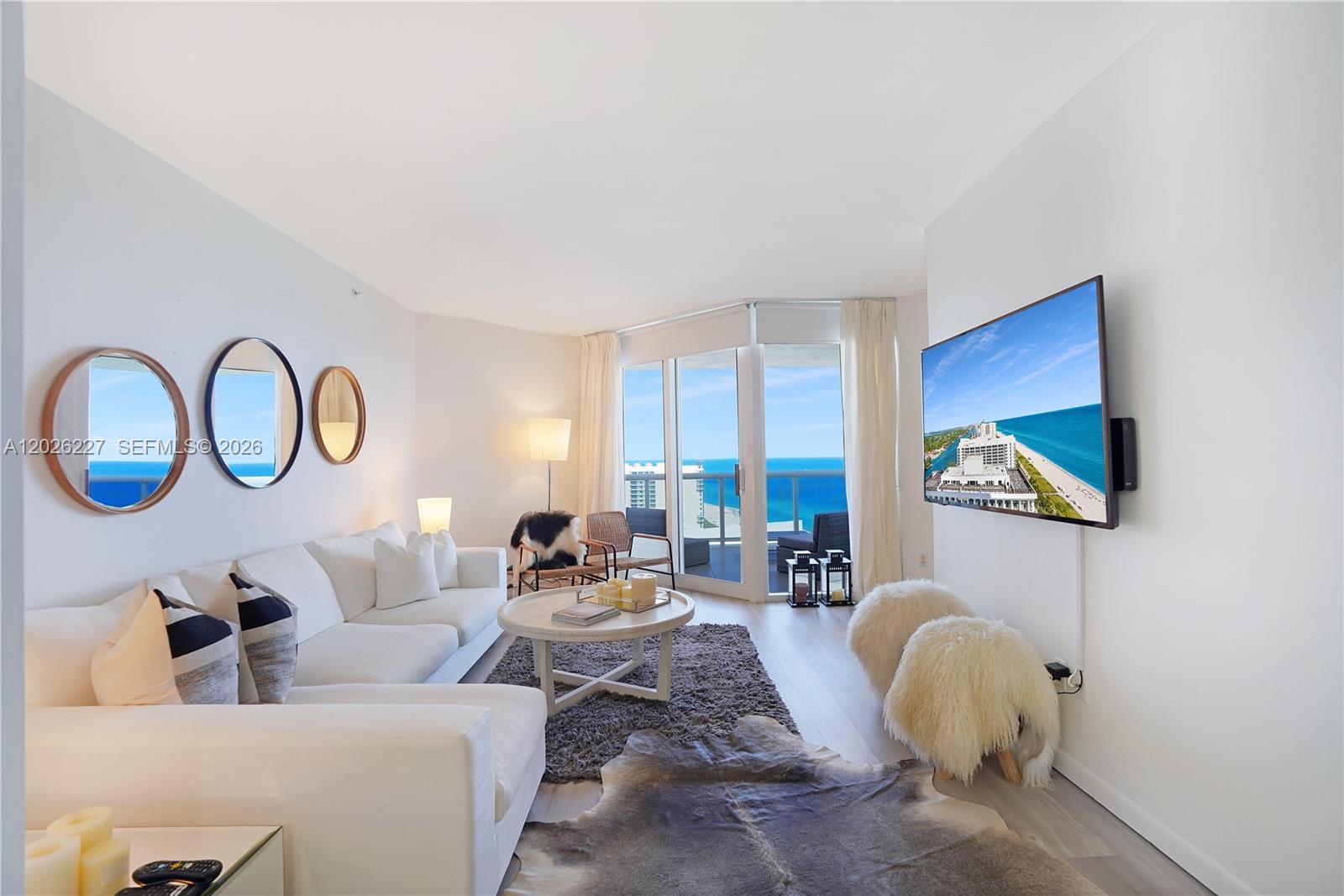 A bright living room features a white sectional, a television, and a balcony overlooking the ocean — 4779 Collins Ave # 2908, Miami Beach FL 33140, MIAMI BEACH, FL