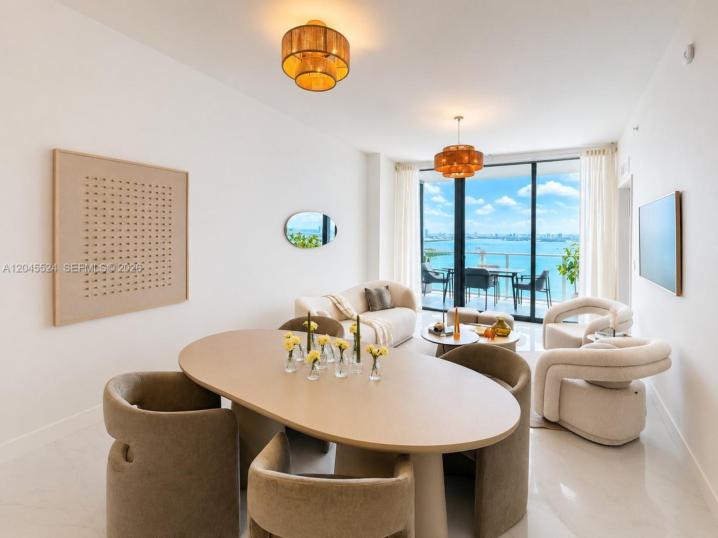 A modern dining and living area features an oval table, neutral furniture, and a balcony view — 711 NE 23rd Ter # 3004, Miami FL 33137, MIAMI, FL