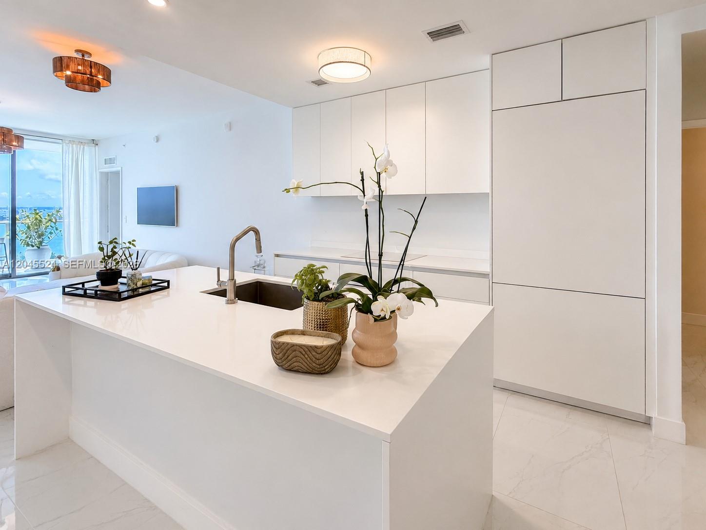 A modern white kitchen features a large island with a sink and minimalist cabinetry — 711 NE 23rd Ter # 3004, Miami FL 33137, MIAMI, FL