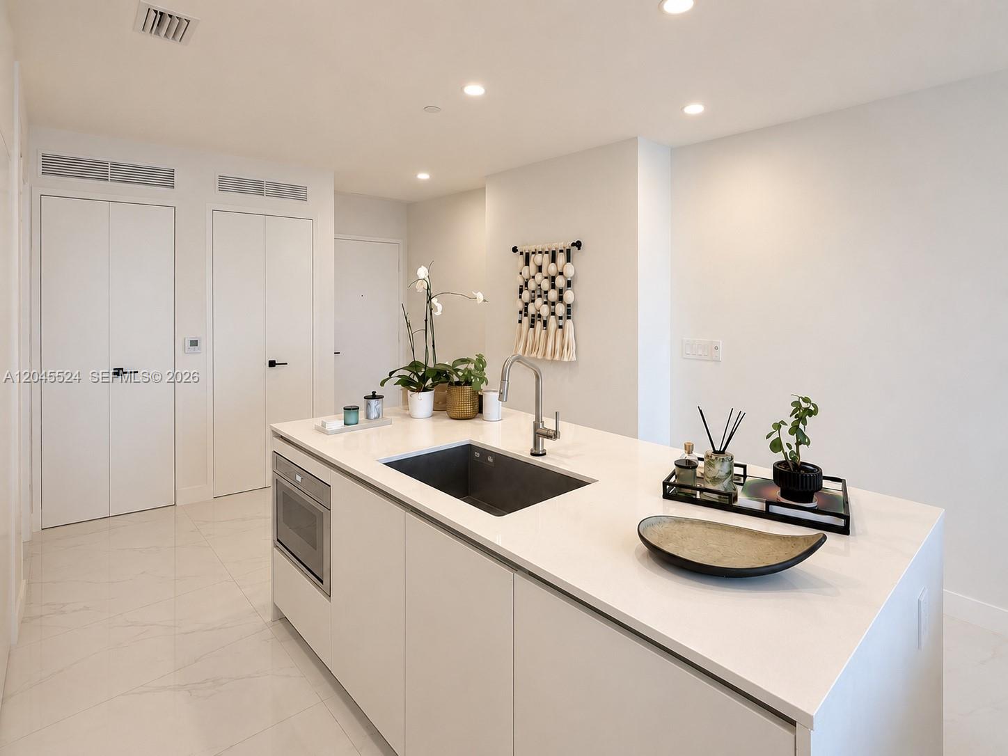 A modern kitchen island with a white countertop and integrated sink sits in a white room — 711 NE 23rd Ter # 3004, Miami FL 33137, MIAMI, FL