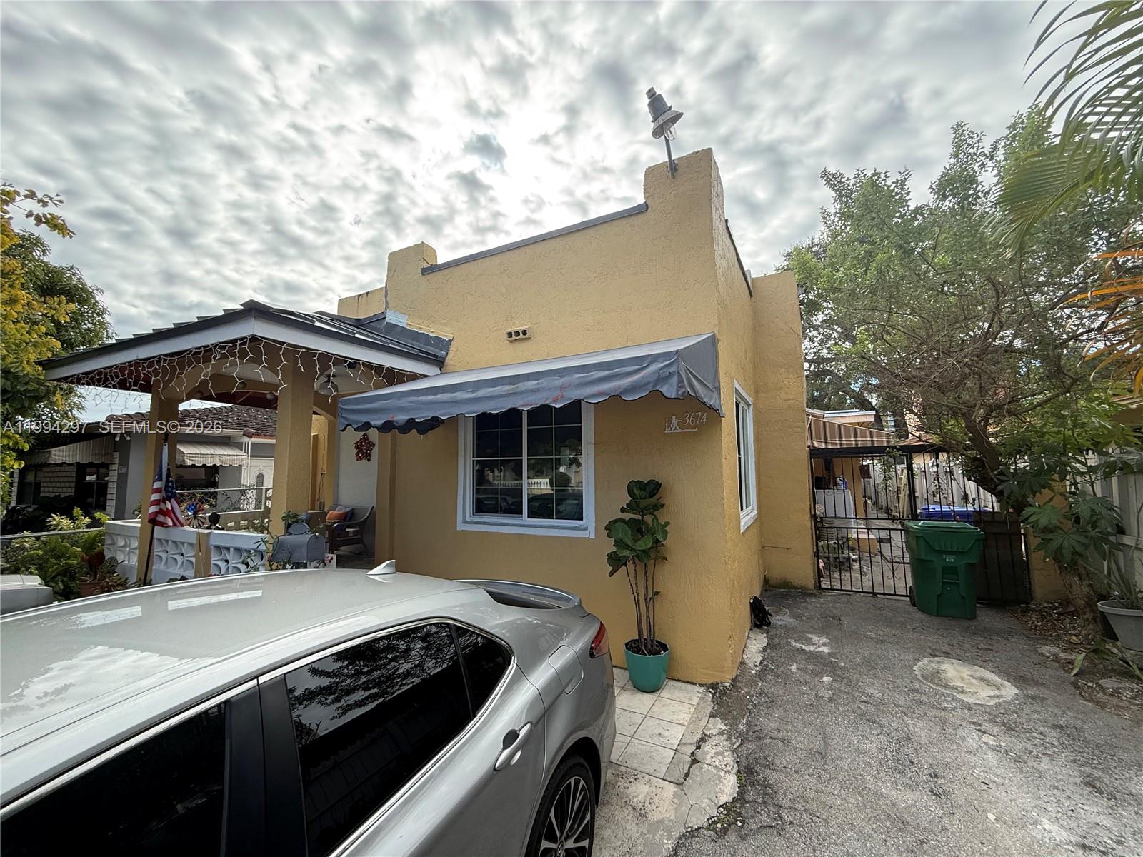 A yellow stucco house with a gray awning and a silver car parked in front — 3674 SW 25th St, Miami FL 33133, MIAMI, FL