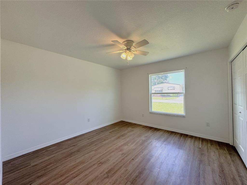 An empty bedroom features white walls, wood-look flooring, a ceiling fan, and a single window — 8225 E ROSKO COURT, FLORAL CITY, FL