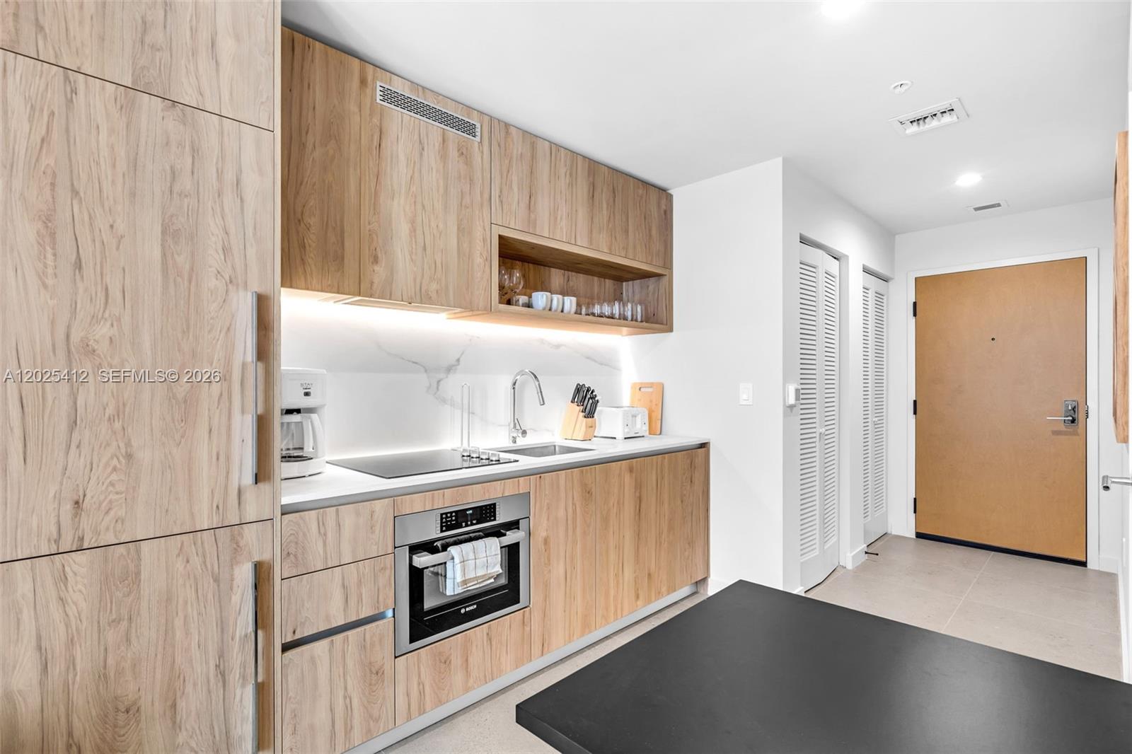 A modern kitchen features light wood cabinetry, a marble backsplash, and a black countertop — 11 NE 6th St # 2608, Miami FL 33132, MIAMI, FL