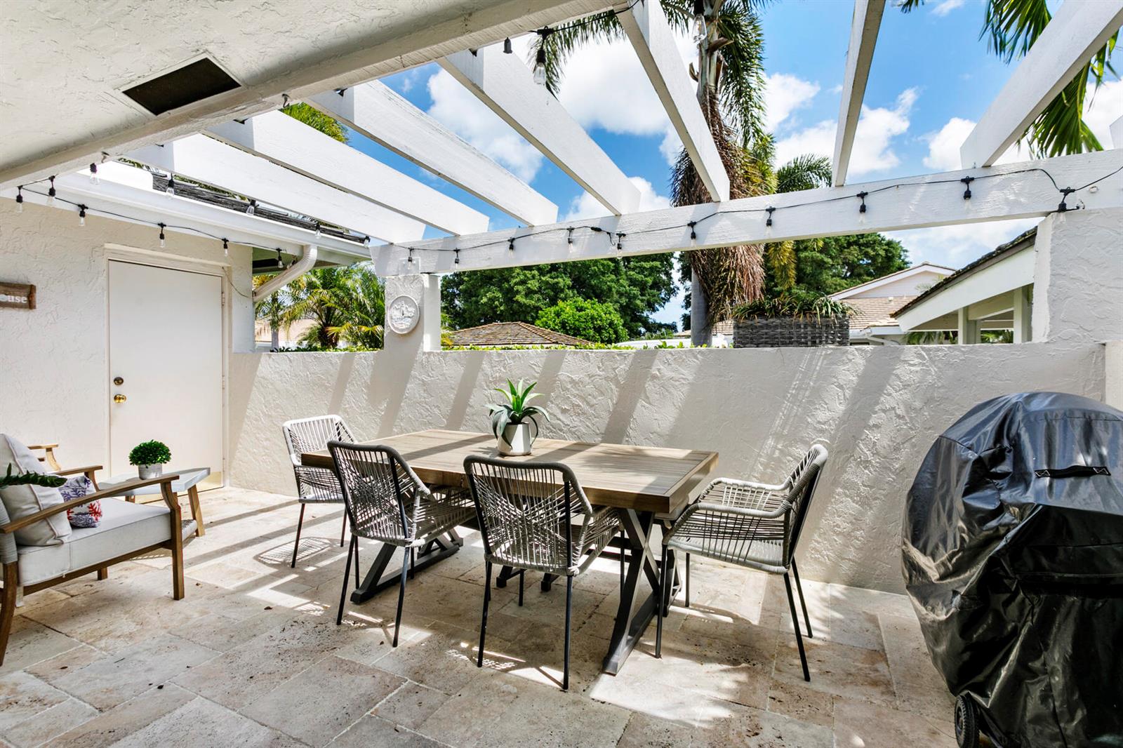 A patio features a wooden dining set, woven chairs, and a pergola under a blue sky — 3616 Freshwater Drive, Jupiter FL 33477, JUPITER, FL