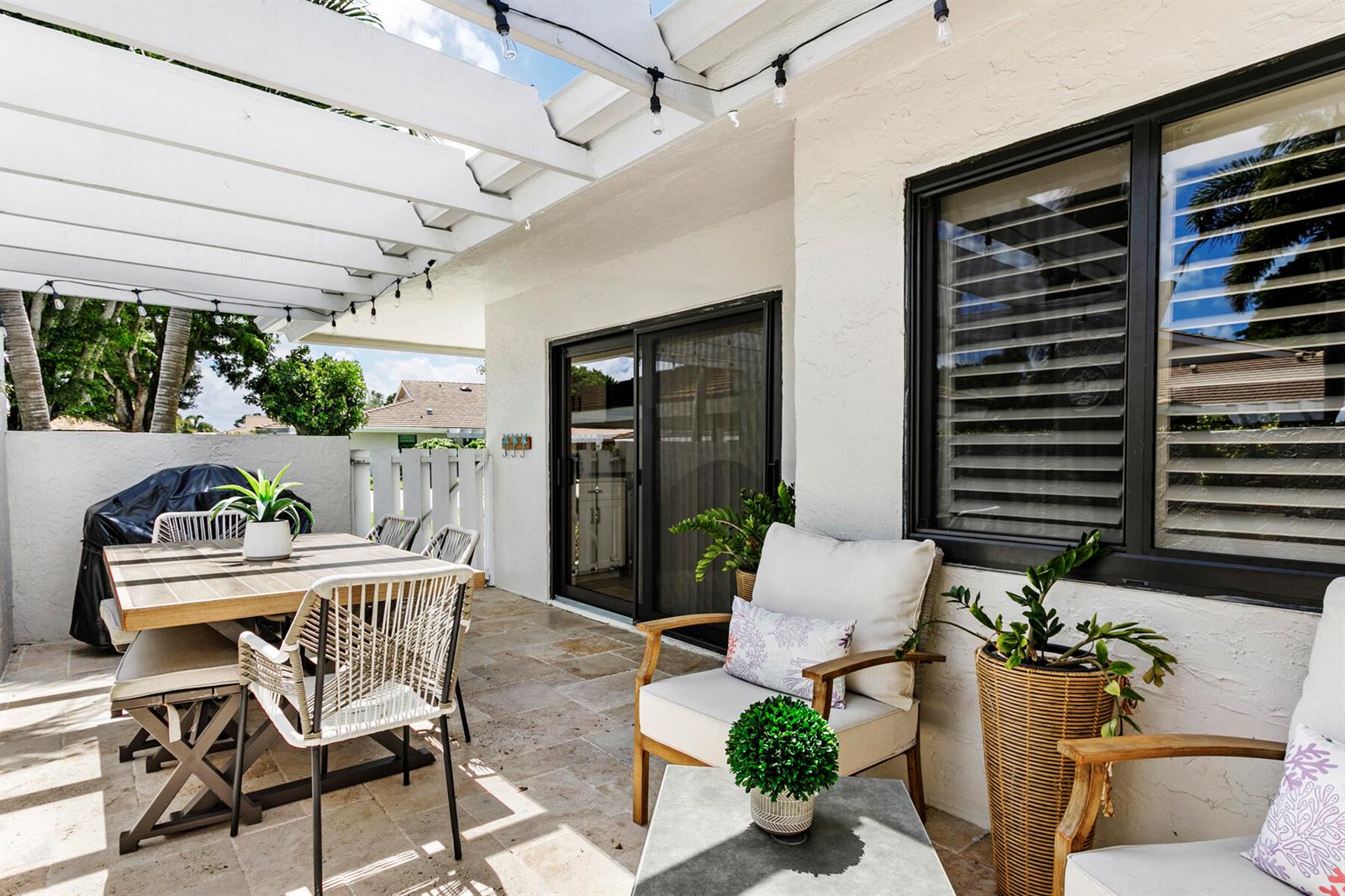 A covered patio features a dining set, lounge chairs, and string lights on a stone floor — 3616 Freshwater Drive, Jupiter FL 33477, JUPITER, FL