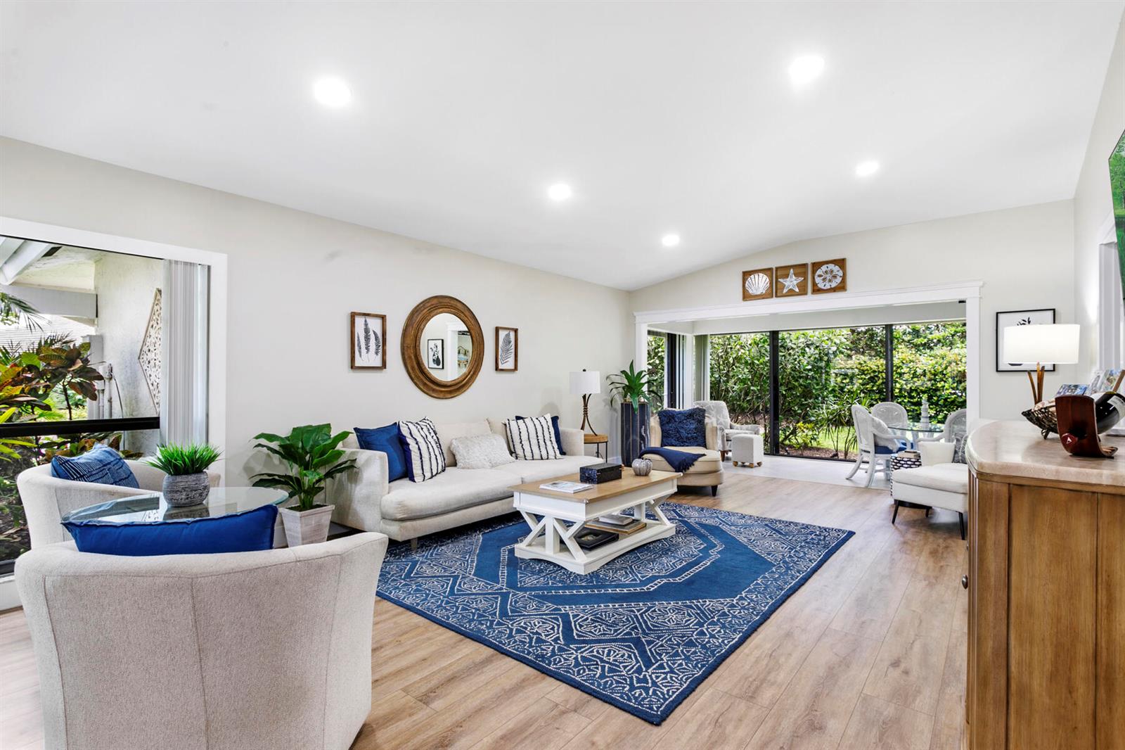 A living room features a blue patterned rug, white sofa, armchairs, and large sliding glass doors — 3616 Freshwater Drive, Jupiter FL 33477, JUPITER, FL