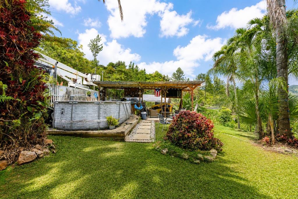 An above-ground pool sits next to a covered patio in a lush, grassy backyard — Carr 156 KM 1.0 BO SABANA SECTOR PUEBLITO, OROCOVIS, PR