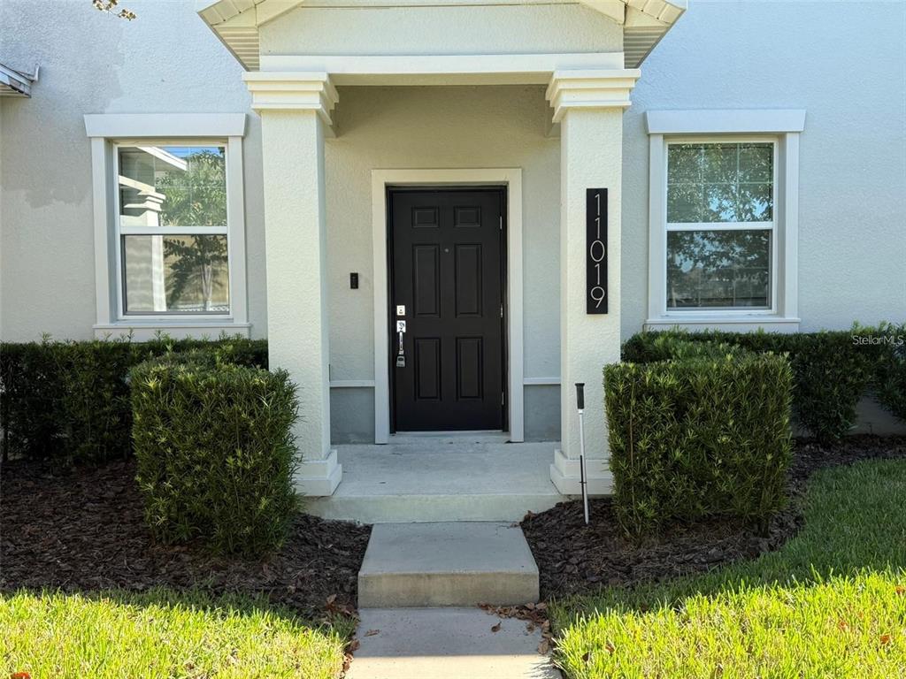 A front entryway features a dark door, a covered porch with two columns, and landscaping — 11019 BOOKMARK LANE, WINTER GARDEN, FL