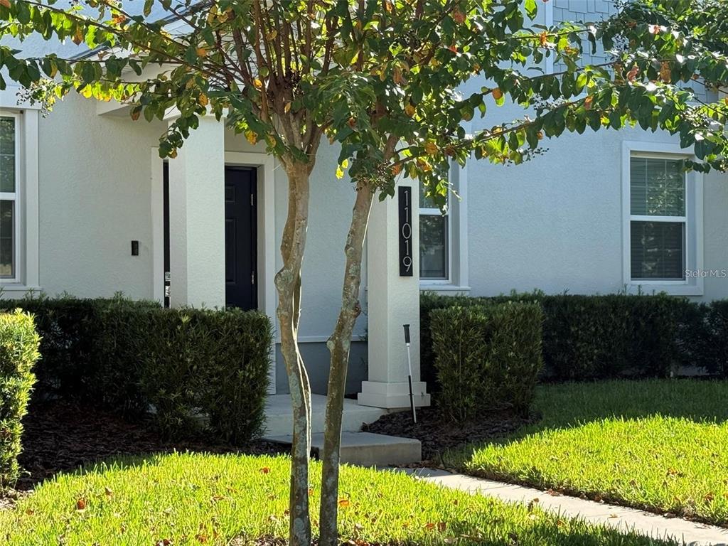 A white house exterior features a front entrance, a tree, and a vertical address sign — 11019 BOOKMARK LANE, WINTER GARDEN, FL