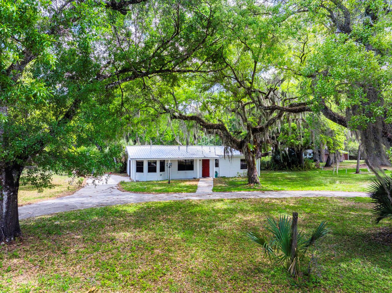 A white single-story house with a metal roof sits under large oak trees — 536 SE 16th Avenue, Okeechobee FL 34974, OKEECHOBEE, FL