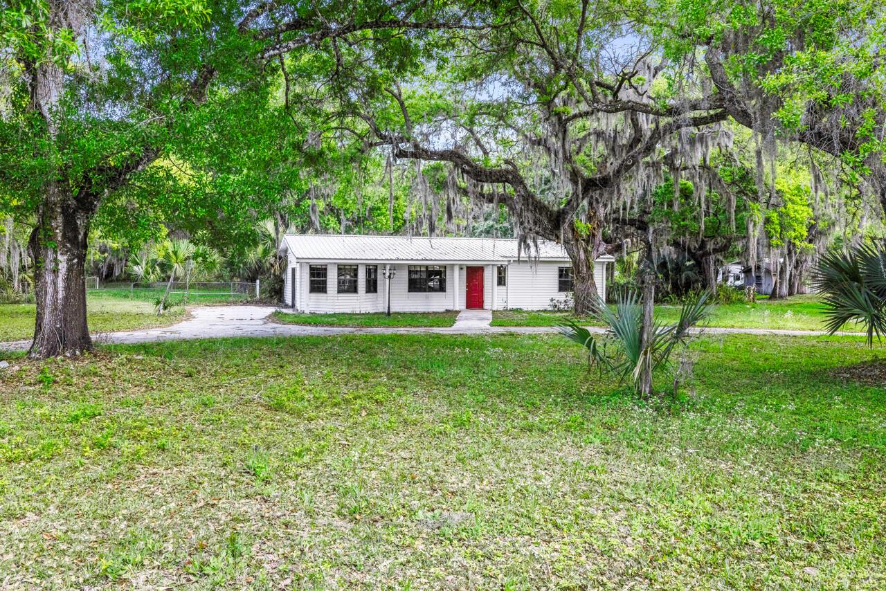 A white, single-story house with a red front door sits on a grassy, tree-filled lot — 536 SE 16th Avenue, Okeechobee FL 34974, OKEECHOBEE, FL
