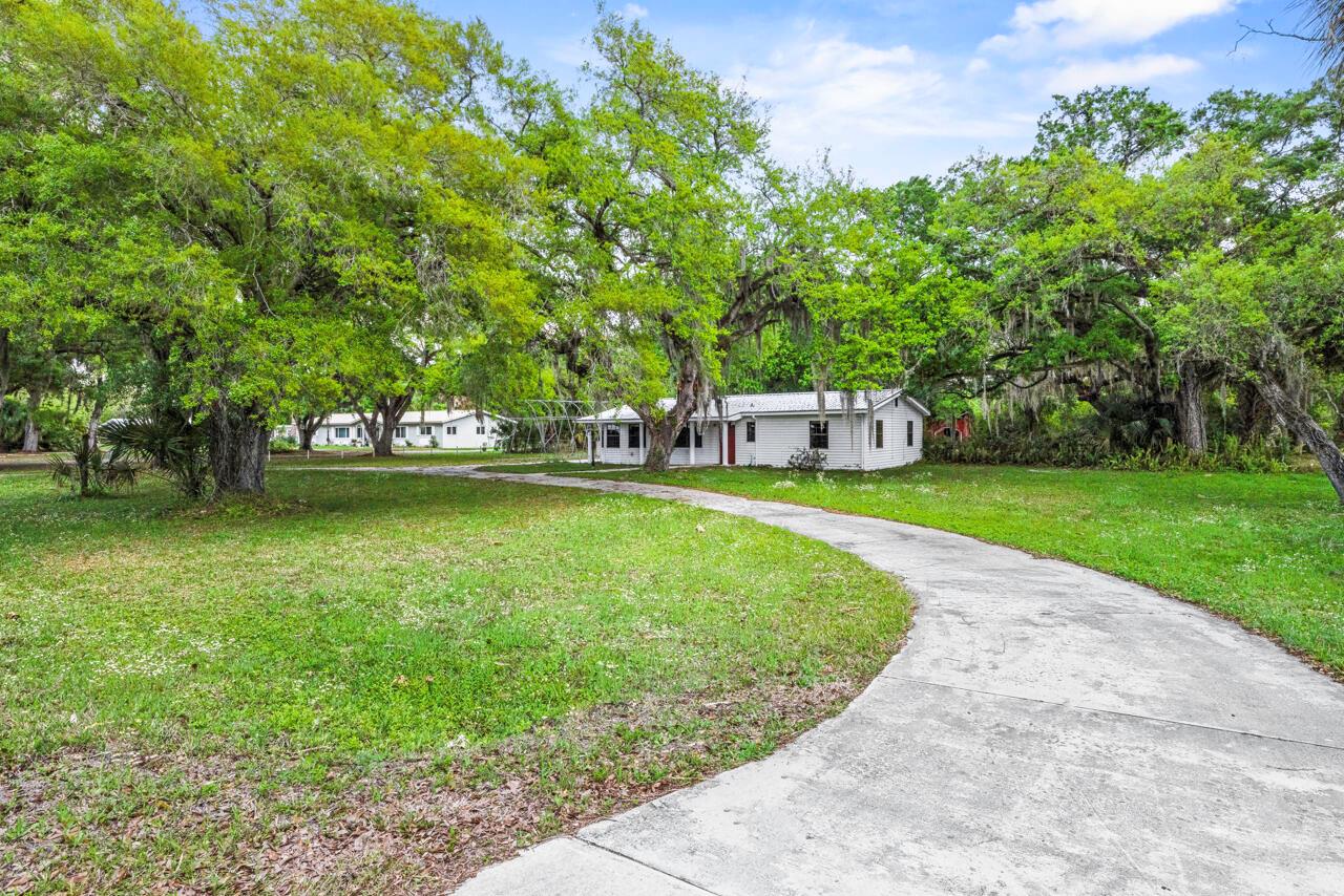 A white single-story house sits at the end of a curved concrete driveway among trees — 536 SE 16th Avenue, Okeechobee FL 34974, OKEECHOBEE, FL