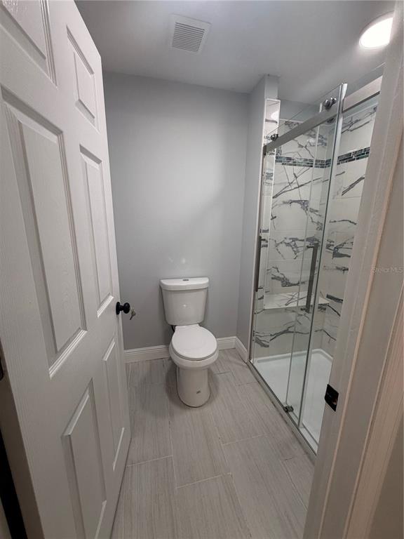 A bathroom features a white toilet, light gray tile flooring, and a glass-enclosed walk-in shower — 319 AVENUE A NE, WINTER HAVEN, FL