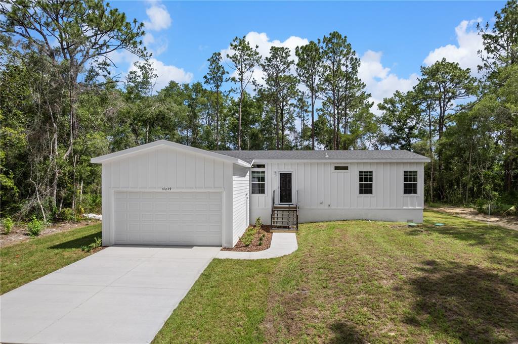 A white single-story house with a garage and a concrete driveway sits in a wooded area — 14249 E RAZORBILL AVENUE, WEEKI WACHEE, FL