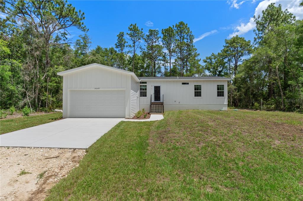 A white single-story house with a garage and a front entrance sits on a lawn — 14249 E RAZORBILL AVENUE, WEEKI WACHEE, FL