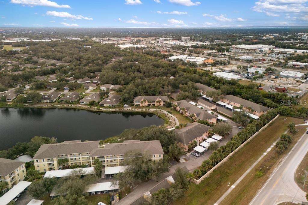 An aerial view shows apartment buildings, a lake, and surrounding residential and commercial areas — 19310 WATER OAK DRIVE UNIT 103, PORT CHARLOTTE, FL