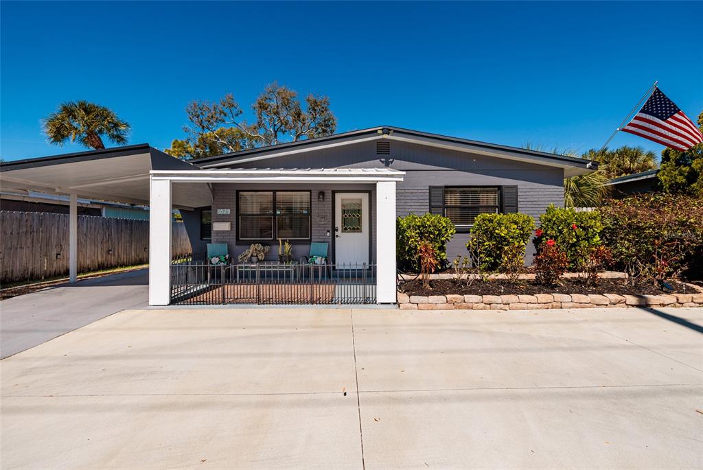 A gray single-story house with a carport, front porch, and an American flag — 8029 22ND AVENUE N, ST PETERSBURG, FL