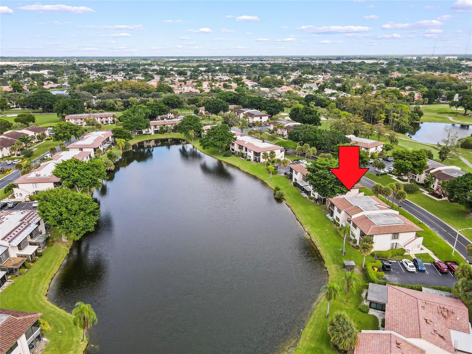 An aerial view shows a multi-story residential building beside a lake with a red arrow — 21649 Juego Circle, Boca Raton FL 33433, BOCA RATON, FL