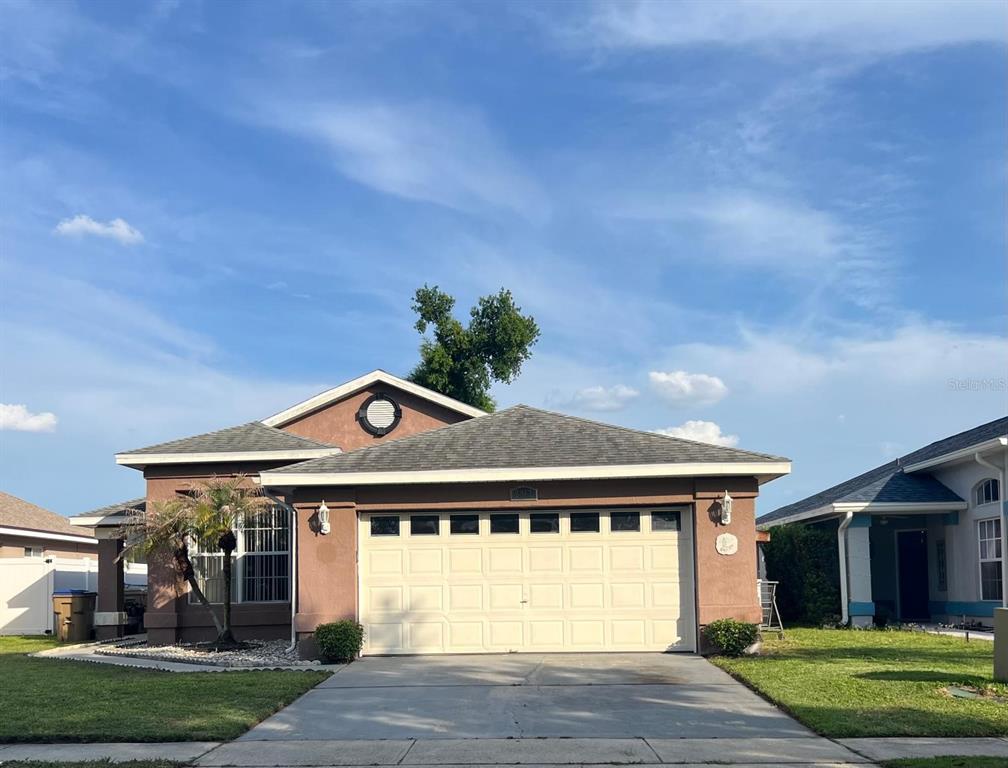 A single-story house with a tan stucco exterior, a two-car garage, and a shingled roof — 2967 STILLWATER DRIVE, KISSIMMEE, FL
