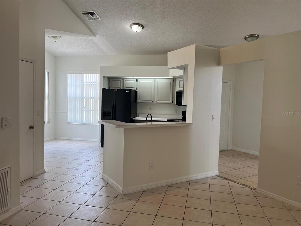 A kitchen with white cabinets and a black refrigerator overlooks a tiled dining area — 2967 STILLWATER DRIVE, KISSIMMEE, FL