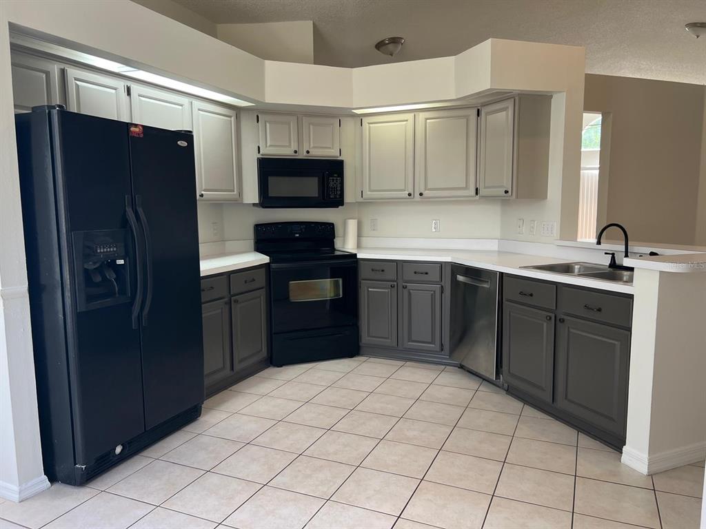 A kitchen features two-toned gray cabinets, black appliances, white countertops, and light-colored tile flooring — 2967 STILLWATER DRIVE, KISSIMMEE, FL