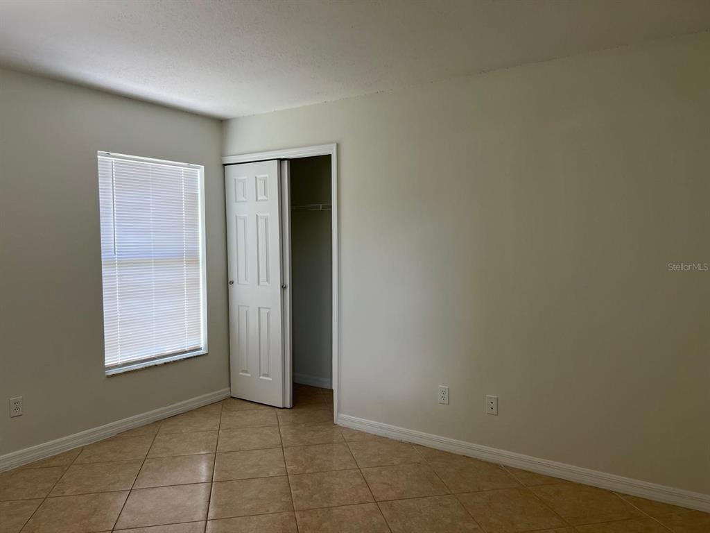 An empty room features beige tile flooring, white walls, a window with blinds, and a closet — 2967 STILLWATER DRIVE, KISSIMMEE, FL