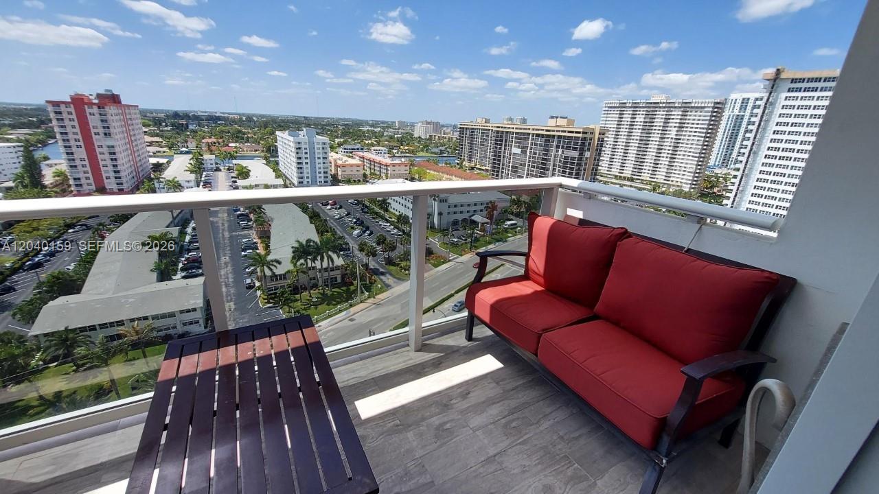 A balcony with a red sofa and a wooden table overlooks a city landscape — 3140 S Ocean Dr # 1510, Hallandale Beach FL 33009, HALLANDALE BEACH, FL