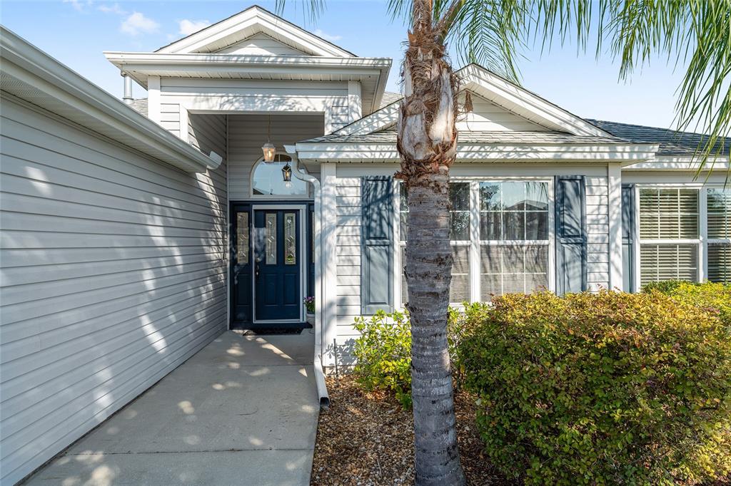 A light-colored house exterior features a dark blue front door and a palm tree — 1529 STRATON WAY, THE VILLAGES, FL