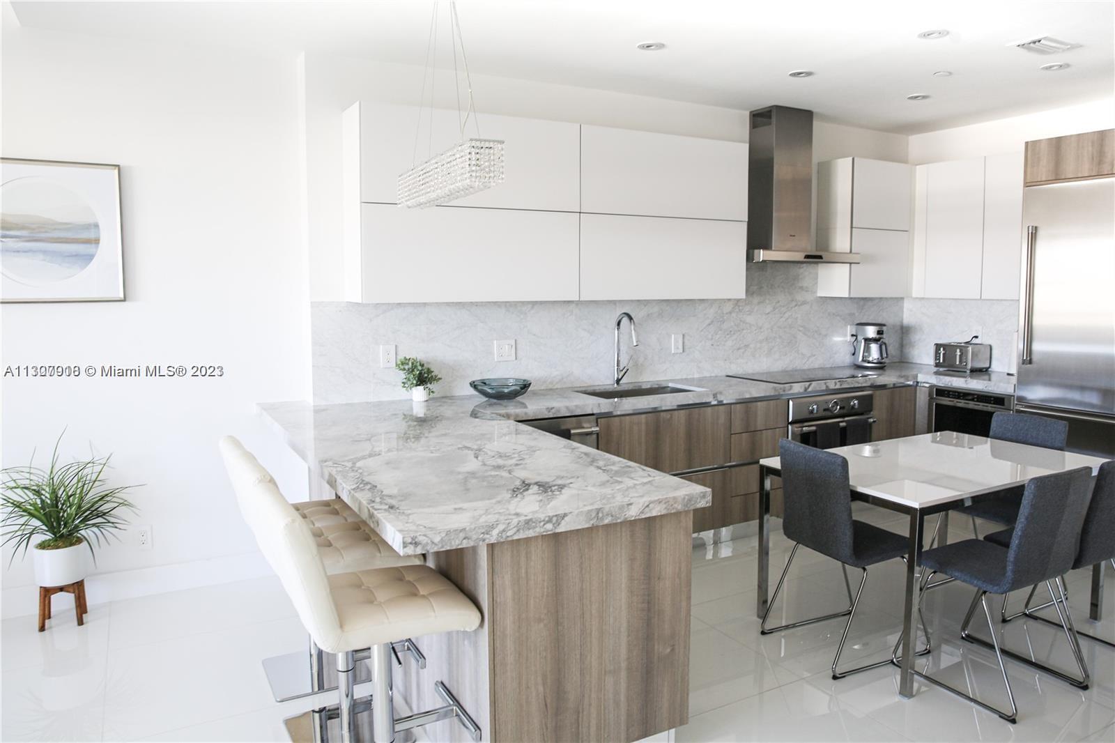 A modern kitchen features white upper cabinets, wood-toned lower cabinets, and marble countertops — 100 Lincoln Rd # 1643, Miami Beach FL 33139, MIAMI BEACH, FL