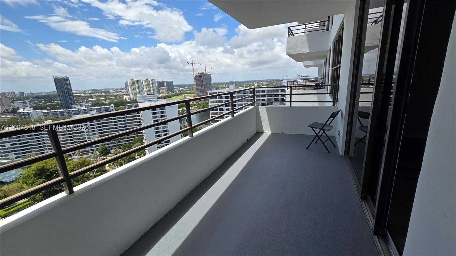 A balcony with a gray floor, metal railings, and a single folding chair overlooks buildings — 2500 Parkview Dr # 2317, Hallandale Beach FL 33009, HALLANDALE BEACH, FL