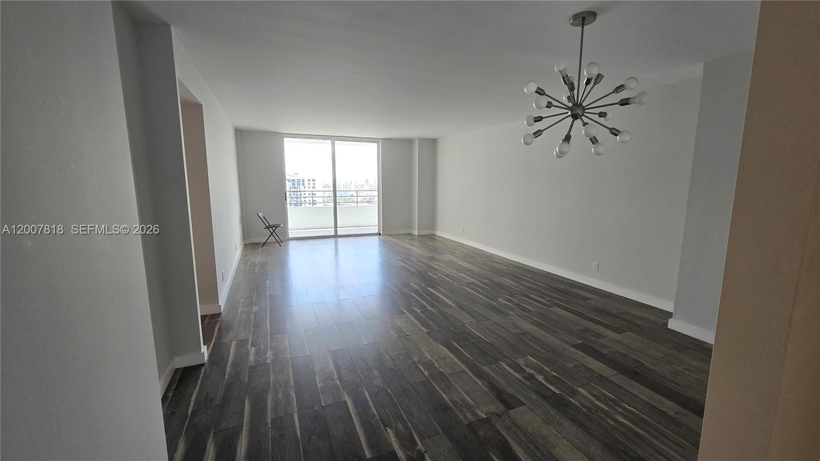 An empty living room features dark wood-look flooring, white walls, and a modern sputnik chandelier — 2500 Parkview Dr # 2317, Hallandale Beach FL 33009, HALLANDALE BEACH, FL