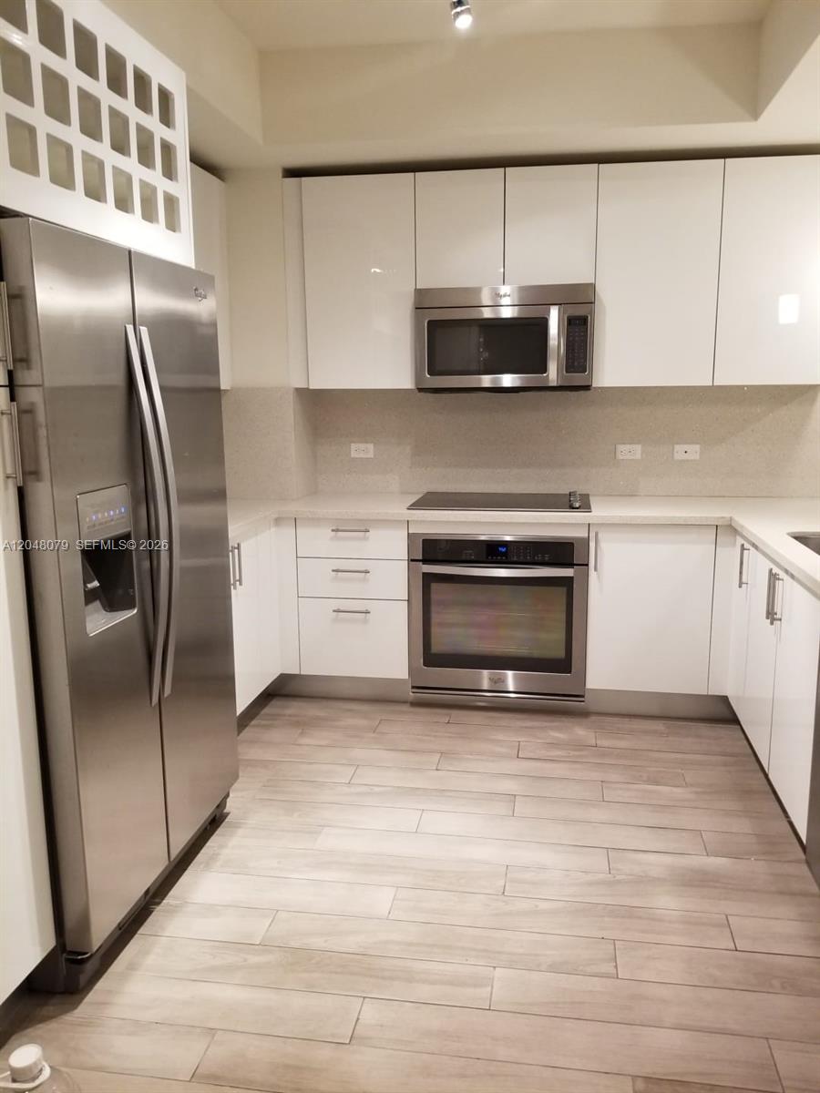 A modern kitchen features white flat-panel cabinets, stainless steel appliances, and light wood-look flooring — 999 SW 1st Ave # 3308, Miami FL 33130, MIAMI, FL
