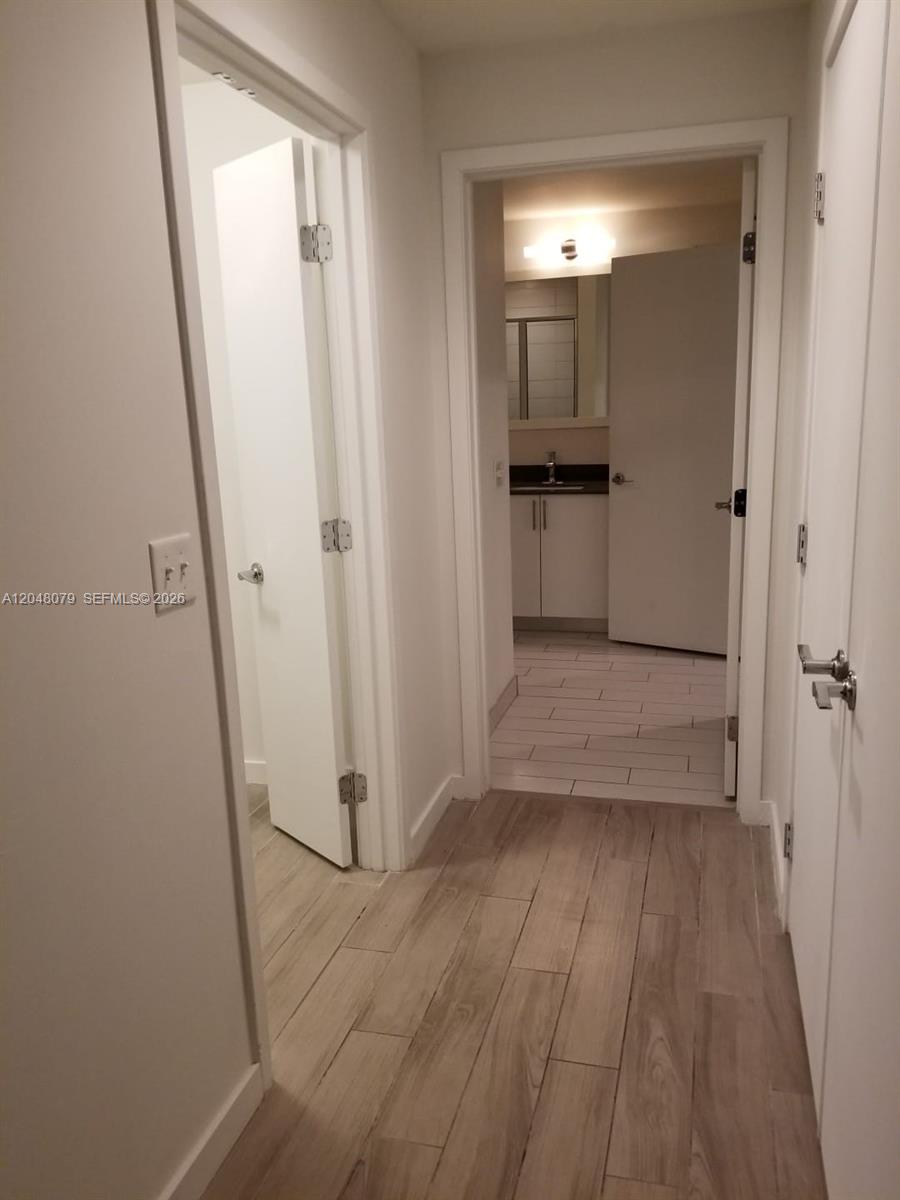 A hallway with light wood-look flooring leads to a bathroom with white cabinets — 999 SW 1st Ave # 3308, Miami FL 33130, MIAMI, FL
